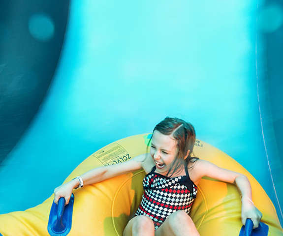 young girl smiling in a tube as she slides down a blue striped water slide.