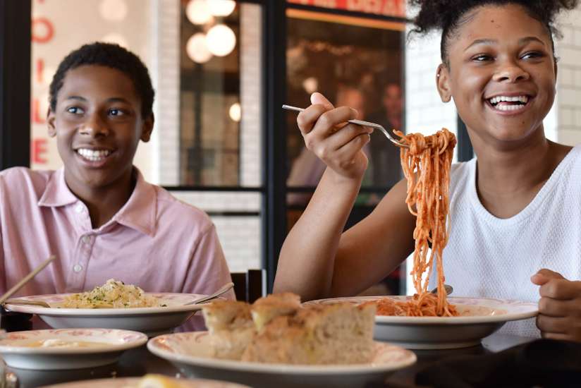 Young girl about to take a giant bite of spaghetti at Sortino's Italian Kitchen.
