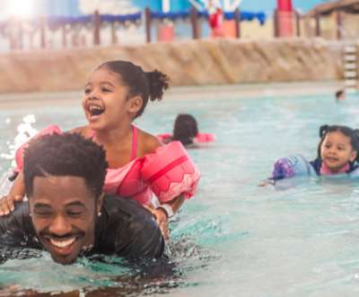 Girl sitting on dad's back in the Wave Pool.