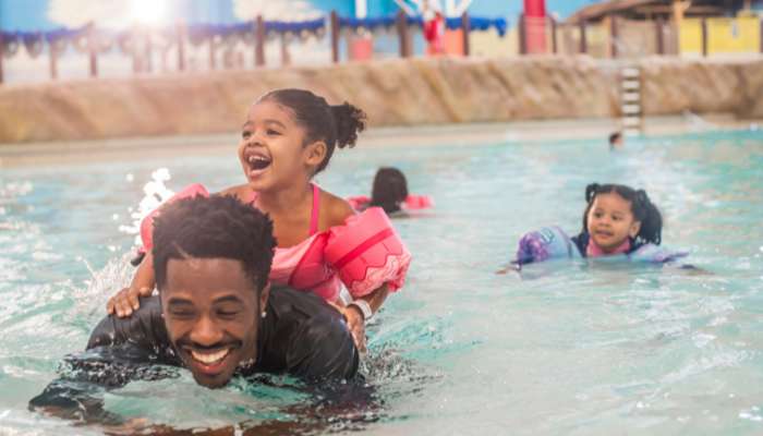 Girl sitting on dad's back in the Wave Pool.