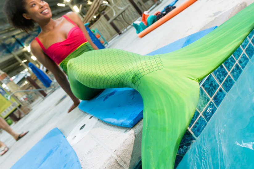 a woman wearing a mermaids tail, sitting at the edge of the pool.