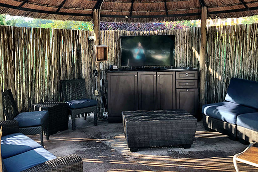 Overview of the outdoor bungalow. Includes table, chairs, tv, and a couch. It's outside!