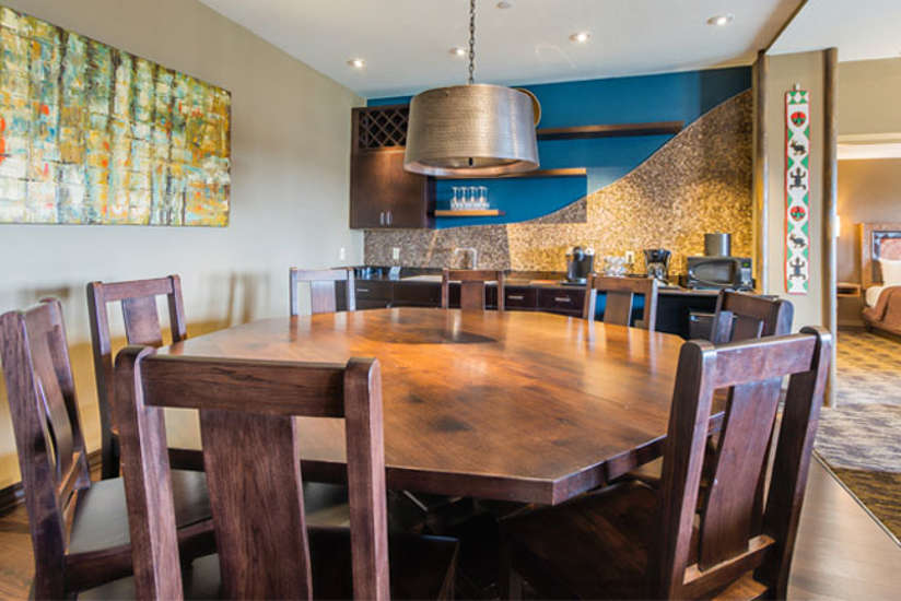 an overview of inside the Penthouse Suite's dining room with big wooden table and chairs and a mini bar area.