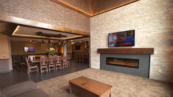 an overview of inside the Big Five Suite. Consists of a kitchen, a large dining area, a couch, fireplace, tv, and large stone wall.