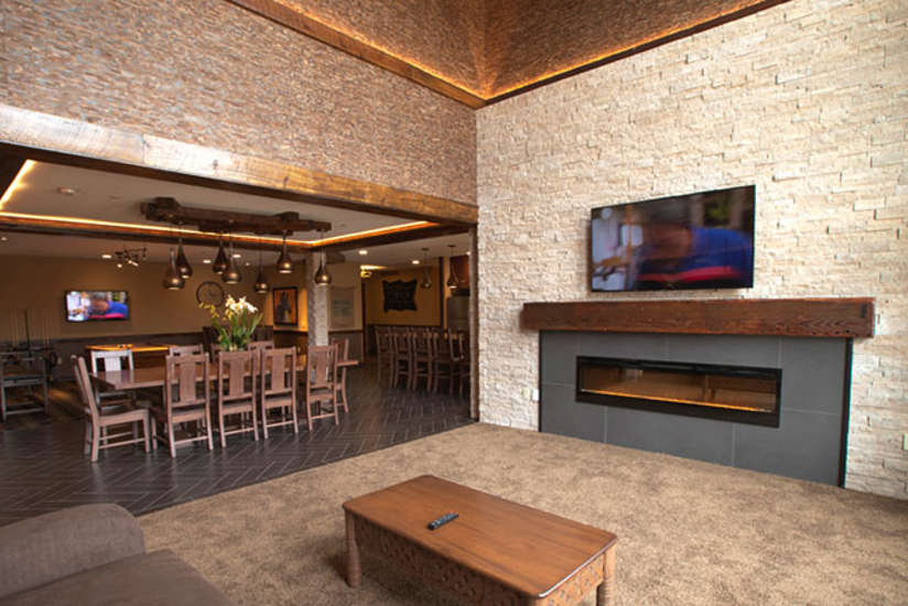 an overview of inside the Big Five Suite. Consists of a kitchen, a large dining area, a couch, fireplace, tv, and large stone wall.