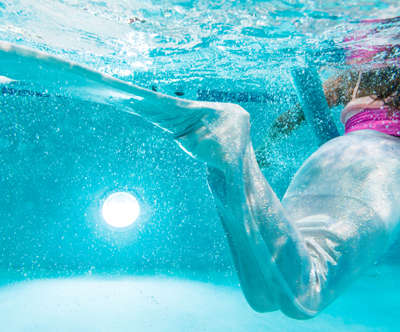 a young girl wearing a mermaids tail and swimming in a pool.