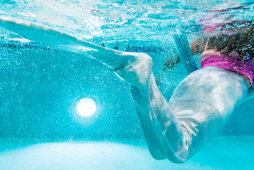 a young girl wearing a mermaids tail and swimming in a pool.