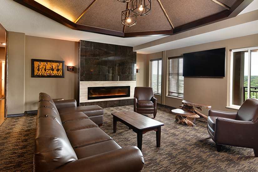 an overview of inside the Penthouse Suite's living room with tv, couch, chair, and large fireplace.
