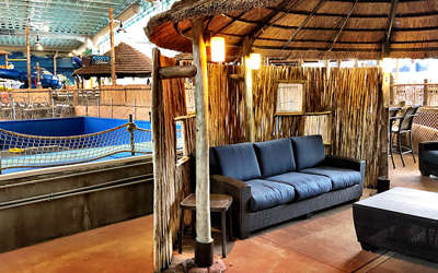 an overview of the surfers cabana. It includes a tv, chairs, couch, and tables. It's right next to the flowrider.