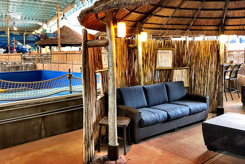 an overview of the surfers cabana. It includes a tv, chairs, couch, and tables. It's right next to the flowrider.