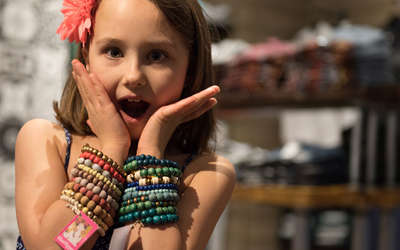 a young girl with a flower in her hair excitedly trying on bracelets