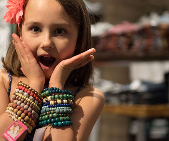 a young girl with a flower in her hair excitedly trying on bracelets