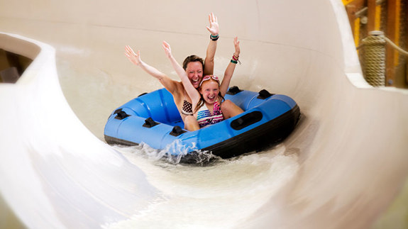 A mom and daughter with their arms up on a water slide