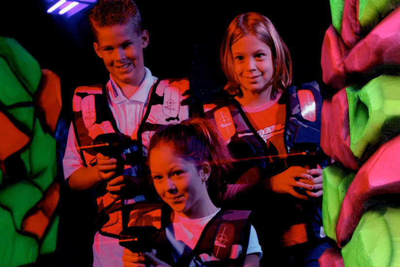 three kids playing laser tag, hiding behind a rocklike structure