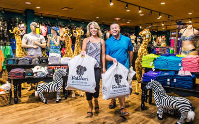 Husband and wife are smiling as they carry large, filled shopping bags out of a Kalahari gift shop