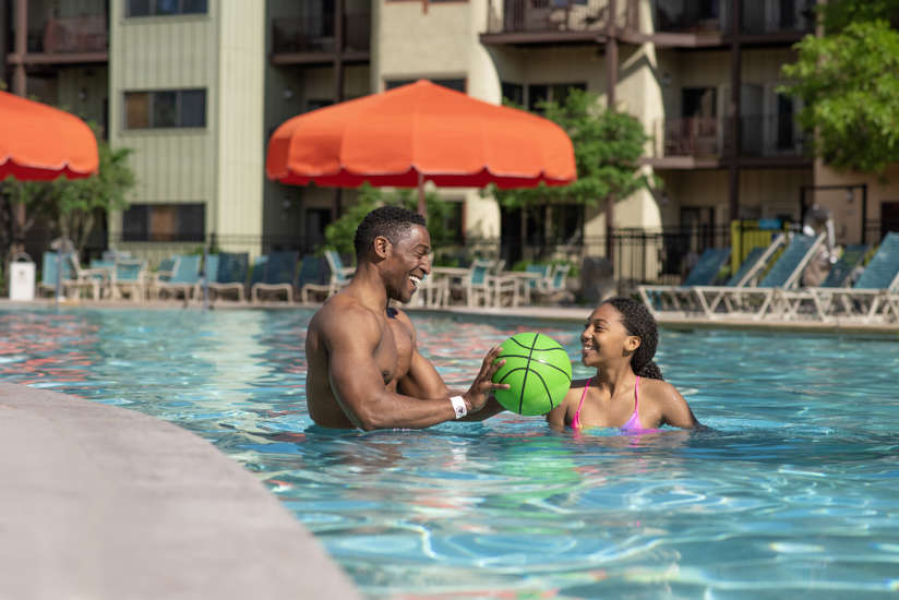 Father and daughter tossing basketball in pool