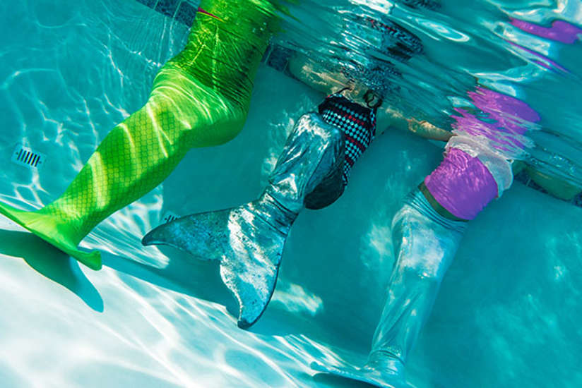 three girls wearing mermaid tails in a pool