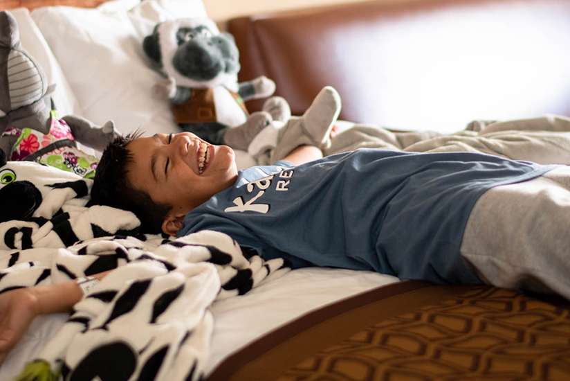 Boy laying in a bed in a Kalahari Guest Room with Kalahari Plush animals and zebra towel along side him