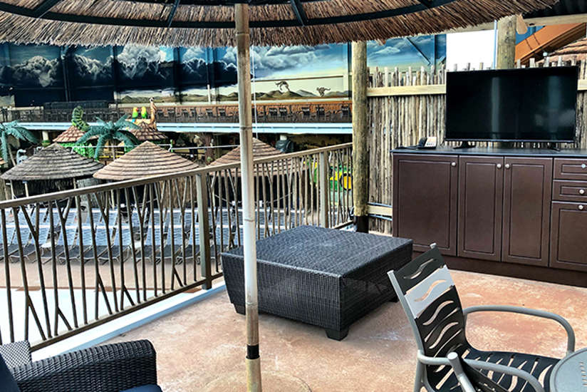 an overview of the wave view cabana. It includes a tv, chairs, couch, and tables. Located right next to the wave pool.