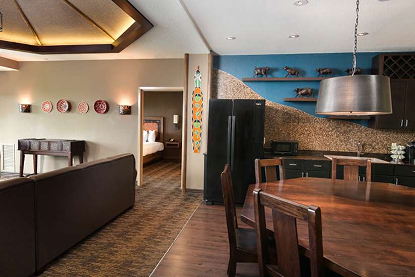 an overview of inside the Penthouse Suite's dining room with big wooden table and chairs and a mini bar area.