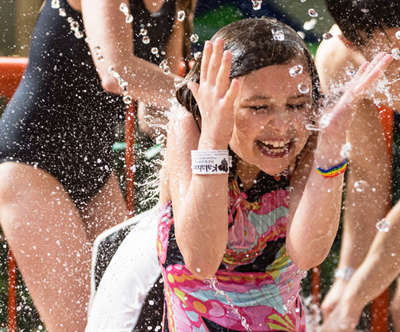 A girl giggling as she is getting splashed in the face with water.