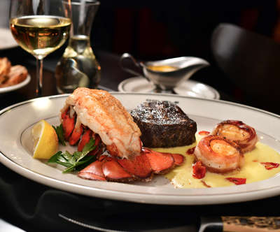 A plate of food containing lobster, steak, and shrimp.
