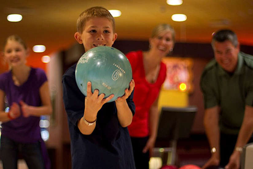 a young boy bowling as his family encourages him