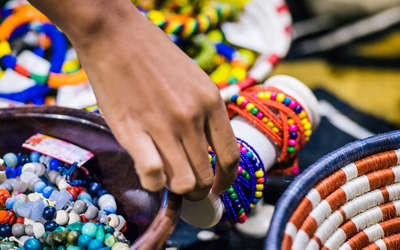 A close-up of some African bracelets with a girl picking one up to try on
