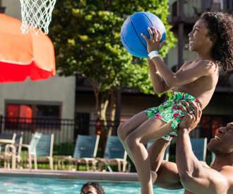 man lifting son to make a basketball hoop in the pool