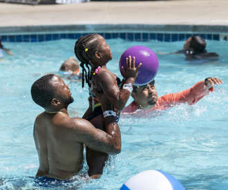 dad helping daughter shoot at the basketball hoop in the water