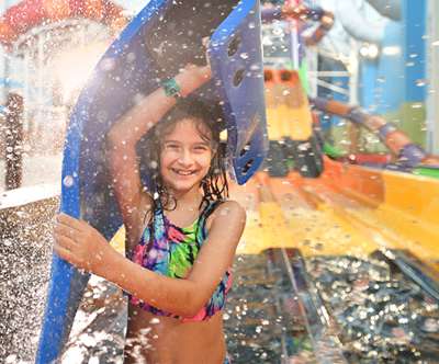 A girl smiling and holding her float device up over her head after sliding down a water slide