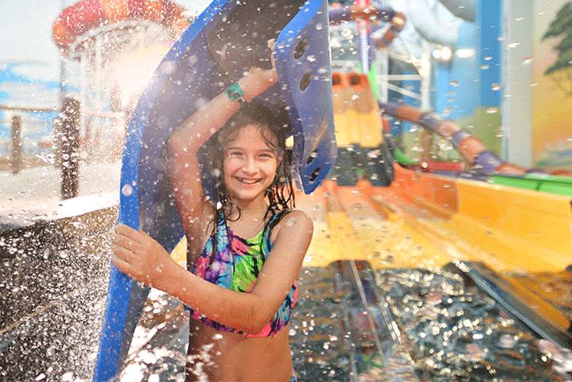 A girl smiling and holding her float device up over her head after sliding down a water slide