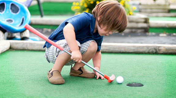 Little boy playing with golf ball and club at minigolf.