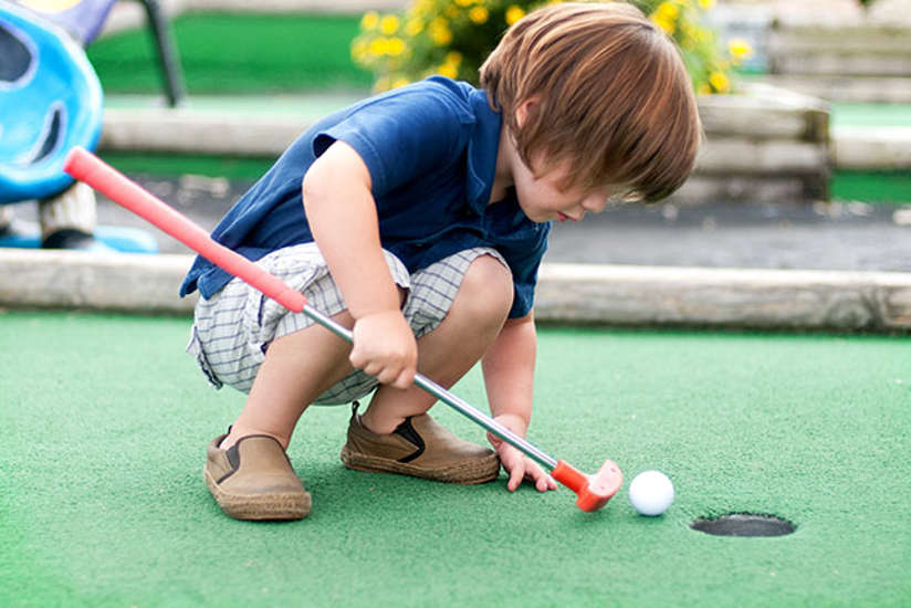 Little boy playing with golf ball and club at minigolf.