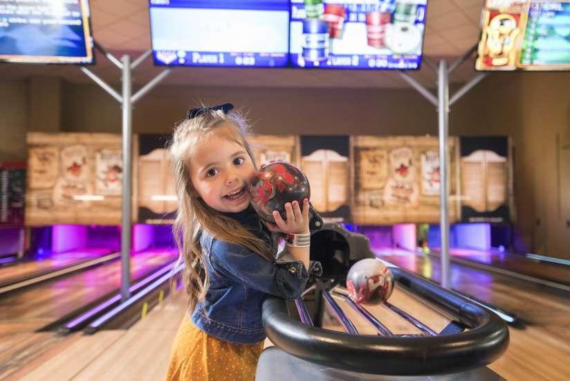 Little girl smiling at camera while holding a bowling ball.