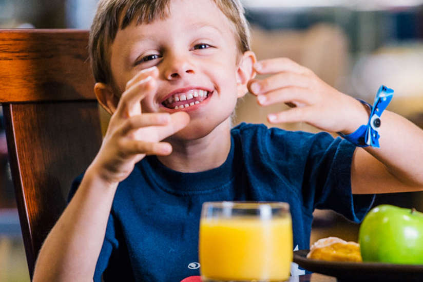 a little boy eating breakfast with some fruit and orange juice