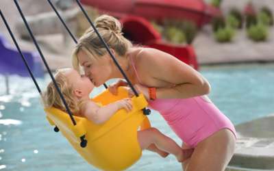 Mom kissing her baby in a water swing in the kid's play area.