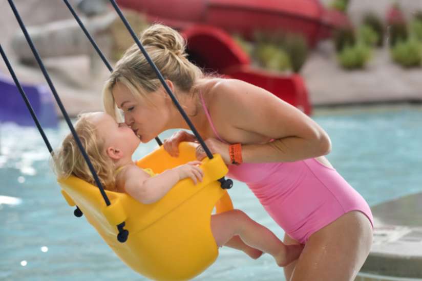 Mom kissing her baby in a water swing in the kid's play area.