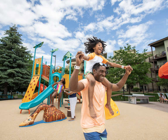 boy on dads shoulders running by the playground