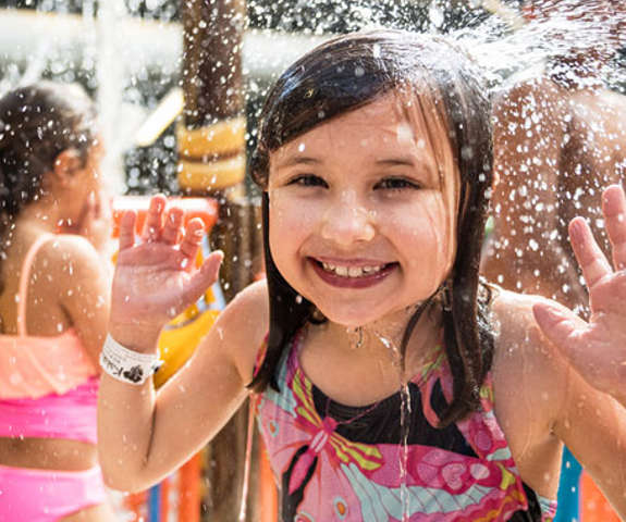 A little girl smiling and laughing as she gets splashed in the face with water.