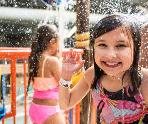 A little girl smiling and laughing as she gets splashed in the face with water.