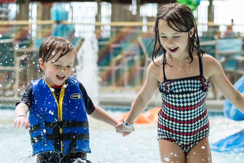brother and sister are running around and playing in the water.