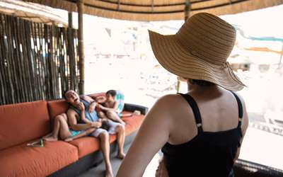 A mother watches as the father and two young children play on a couch in a cabana