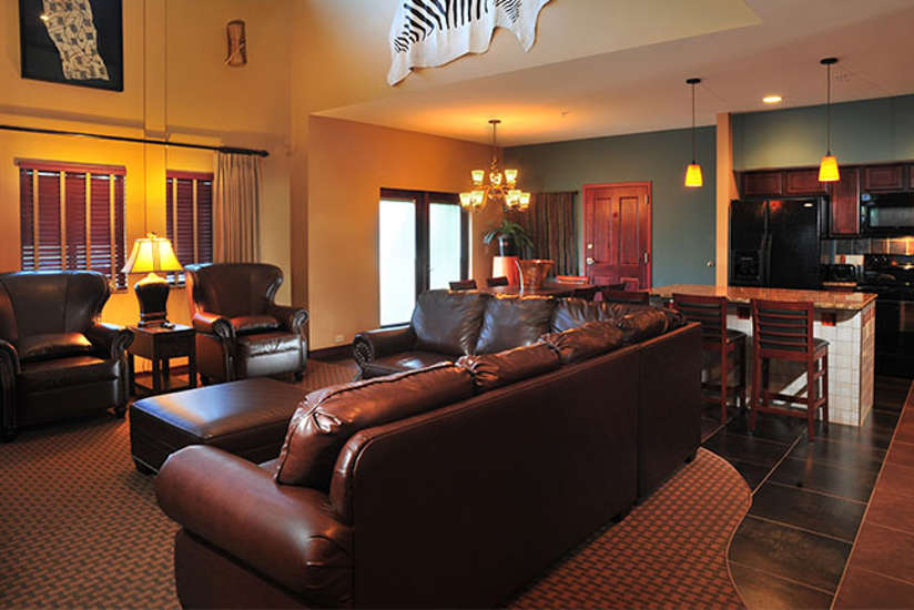 Nyumba Villa living room with a large leather couch and two chairs with a large kitchen in the background