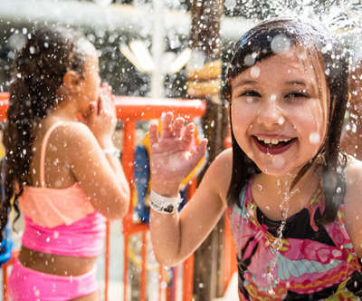 A little girl smiling and laughing as she gets splashed in the face with water.