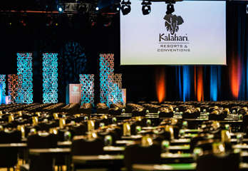 Inside Kalahari's convention center, rows of tables and chairs face a large screen hanging from the ceiling with sculptural lighting behind a podium.